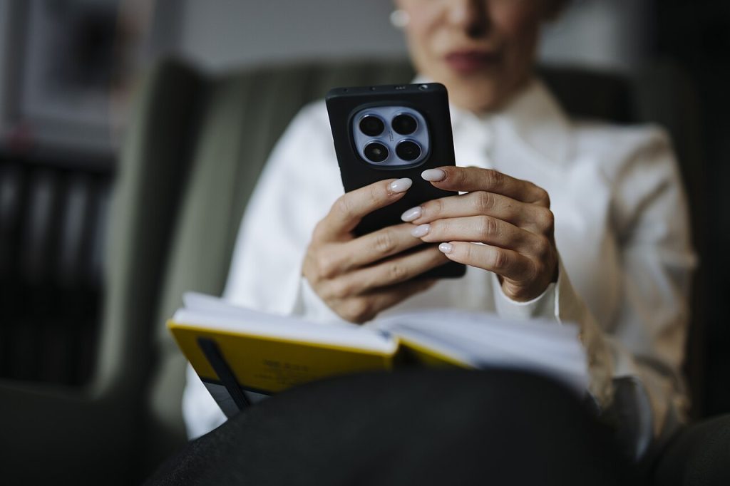 How to Navigate Nex777 Online with Greater Confidence Woman holding a smartphone and a notebook while browsing online